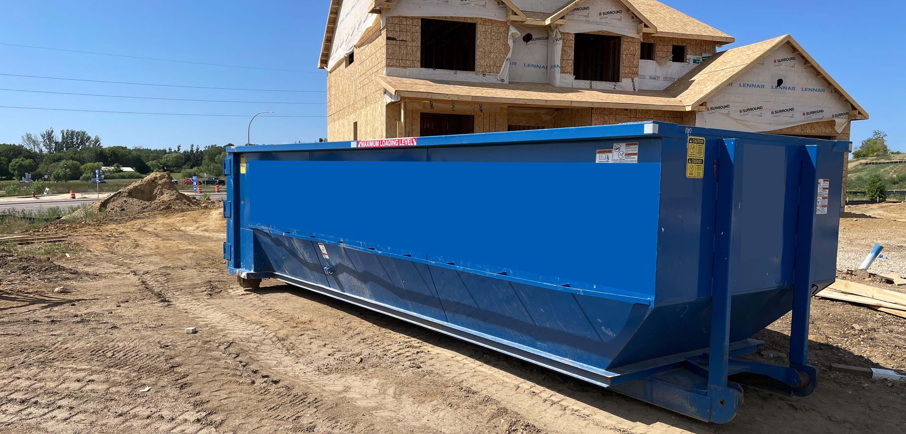 Blue dumpster being placed on the driveway of new home construction area