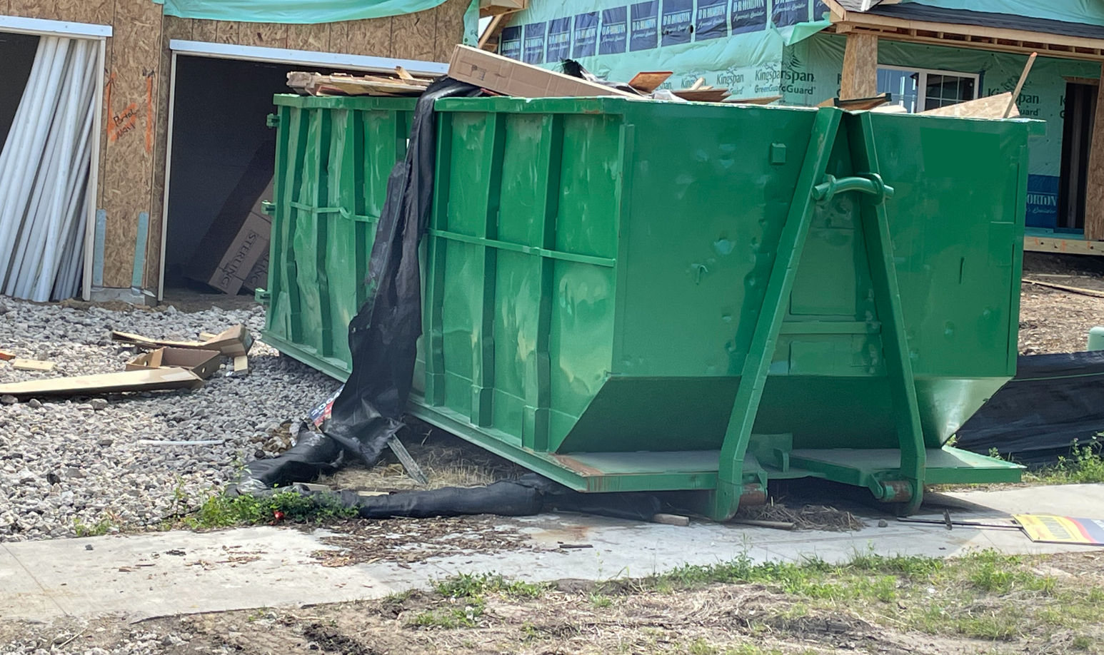 Green dumpster being placed on the driveway of residential area